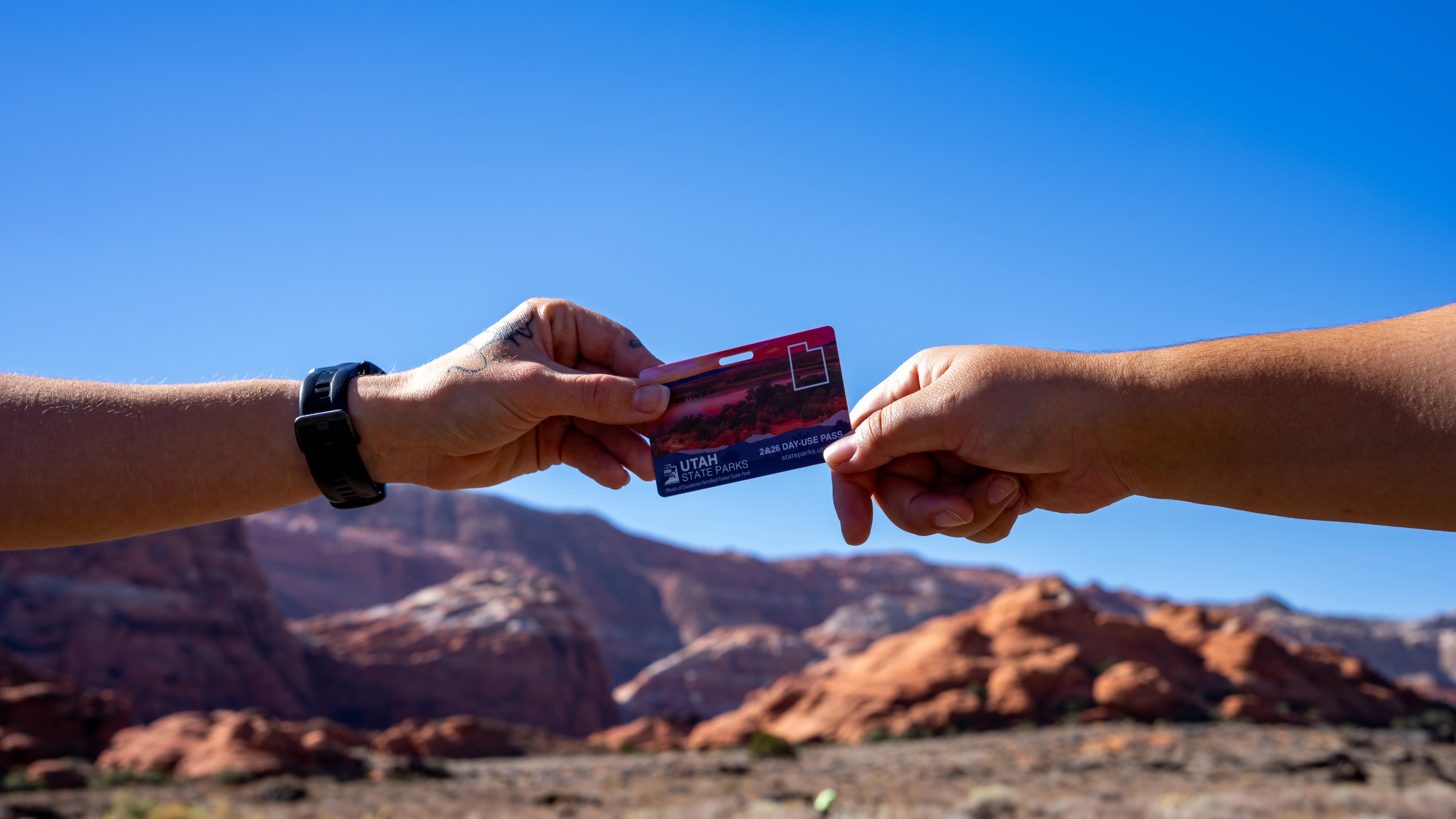 Two hands passing a Utah State Parks day-use pass against a desert landscape.