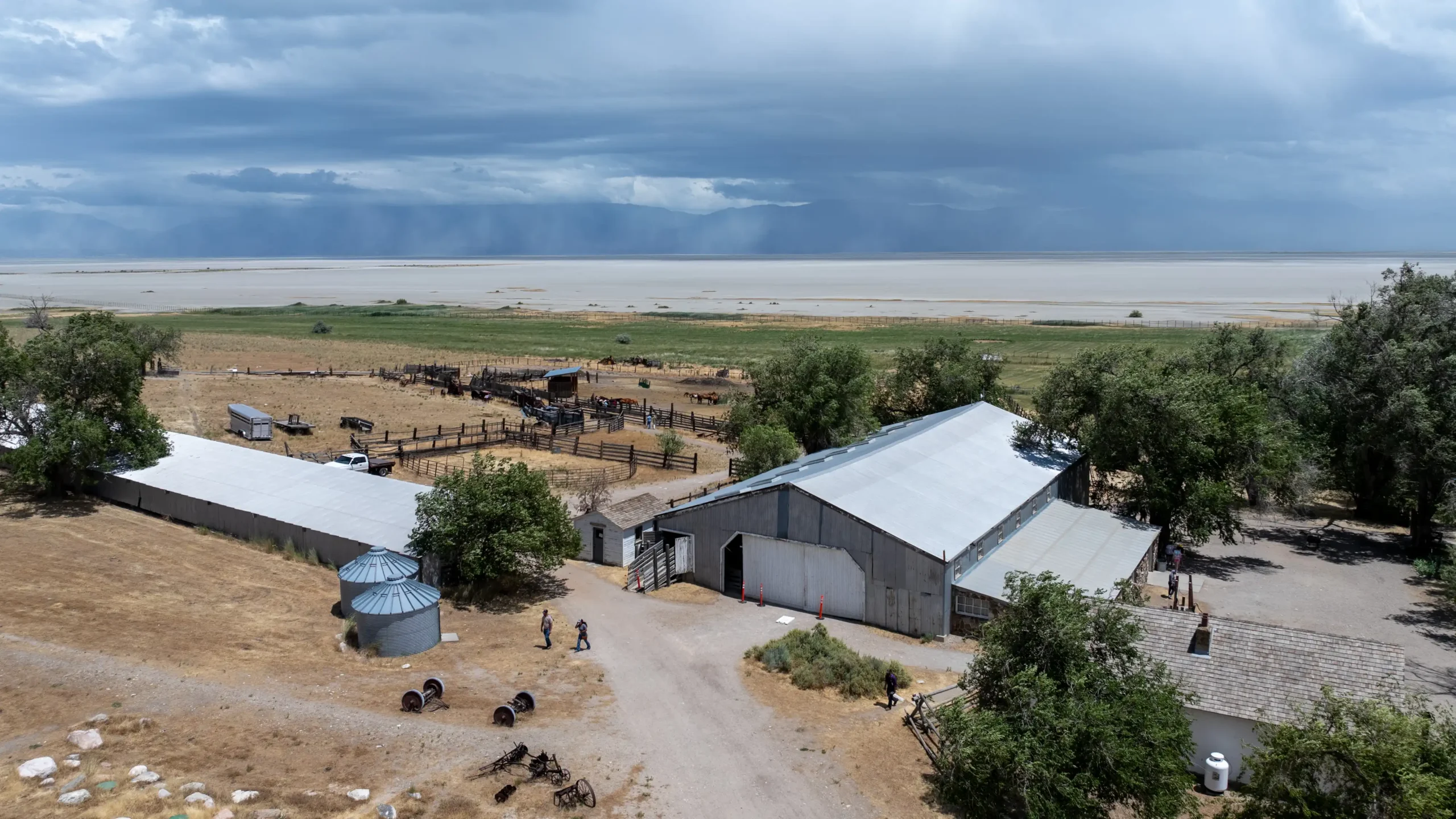 Aerial view of a rural farm with barns, corrals, and people under a cloudy sky.