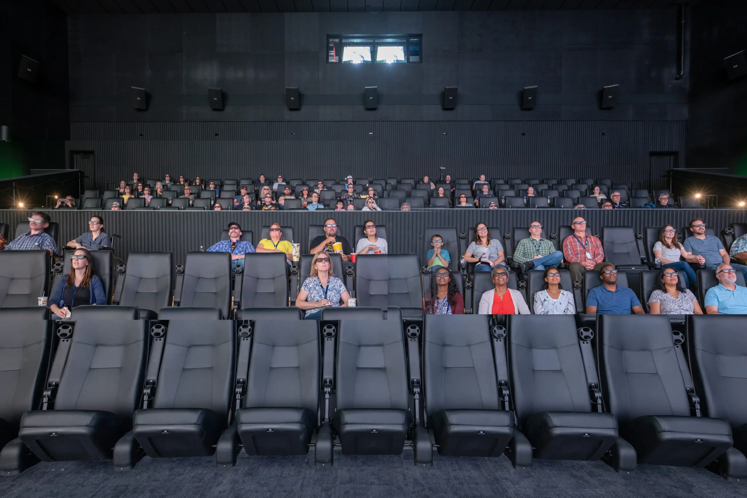People seated in a movie theater, watching a screen in front of them.