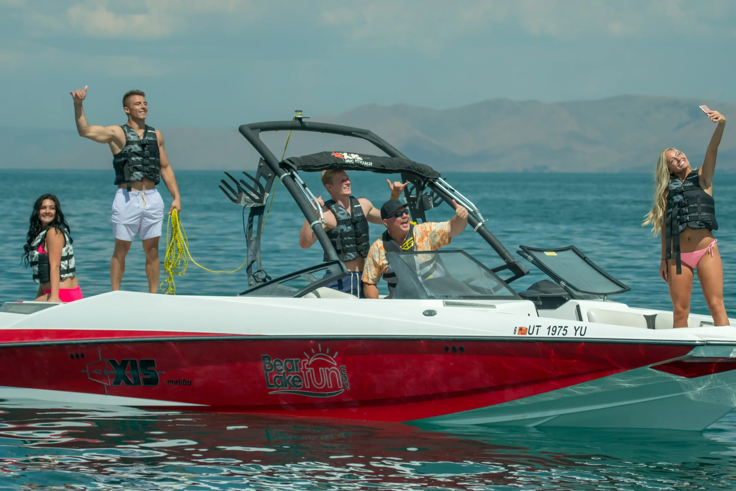 Four people in life vests pose happily on a red and white speedboat on the water.
