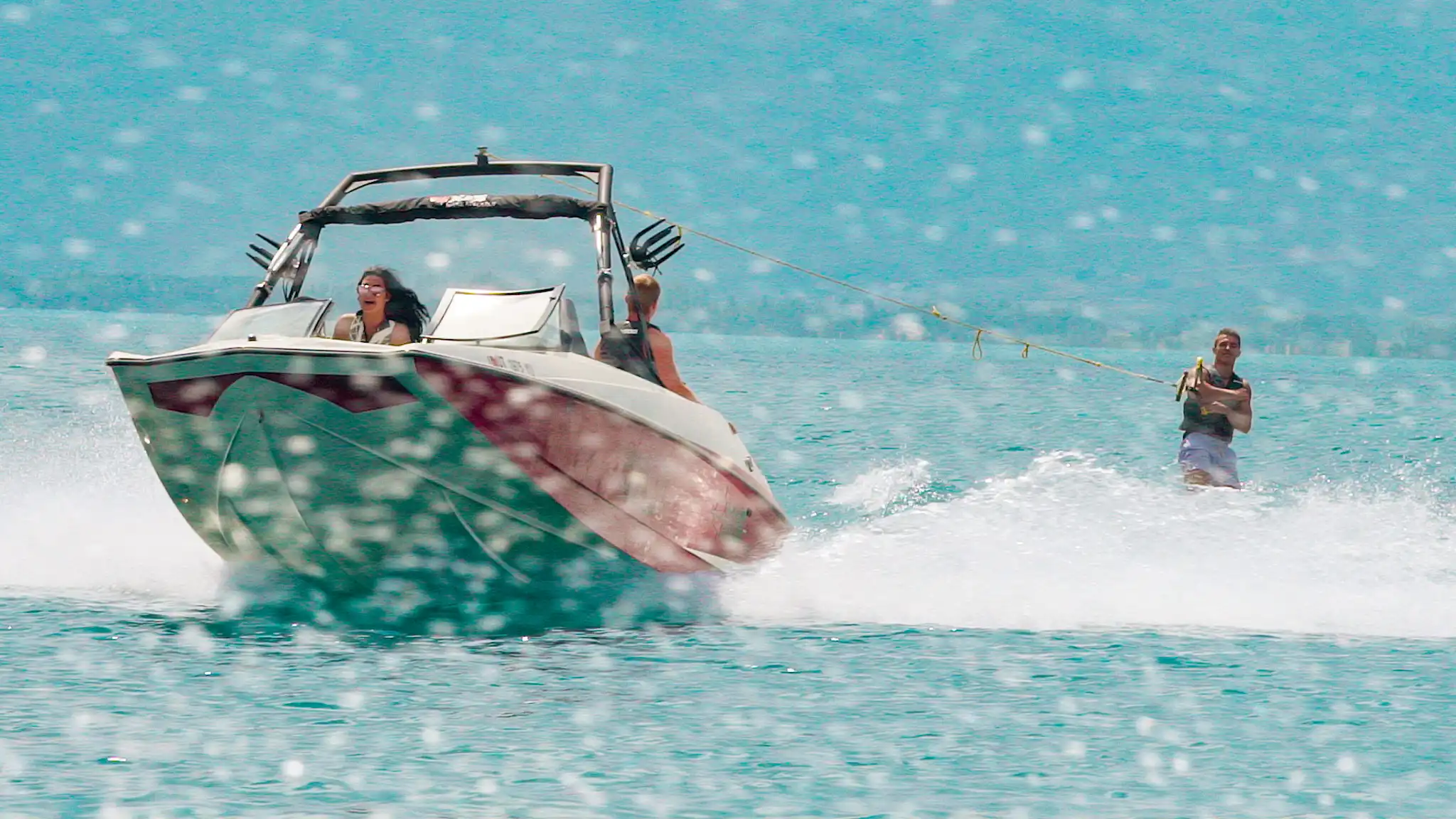 Person water skiing behind a speedboat with two people, water droplets splash in foreground.