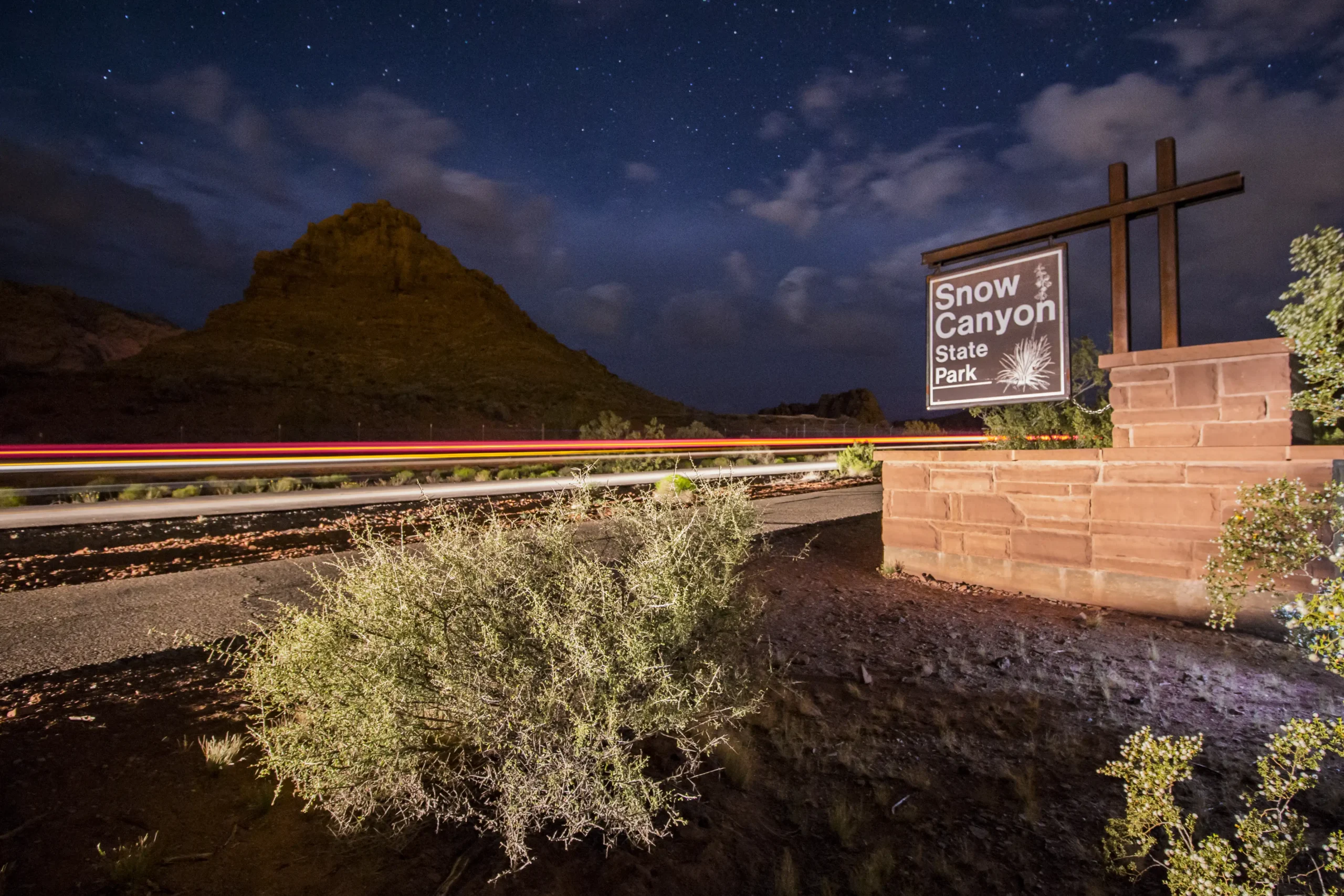 Snow Canyon State Park sign at night with streaks of car lights and mountain in background.