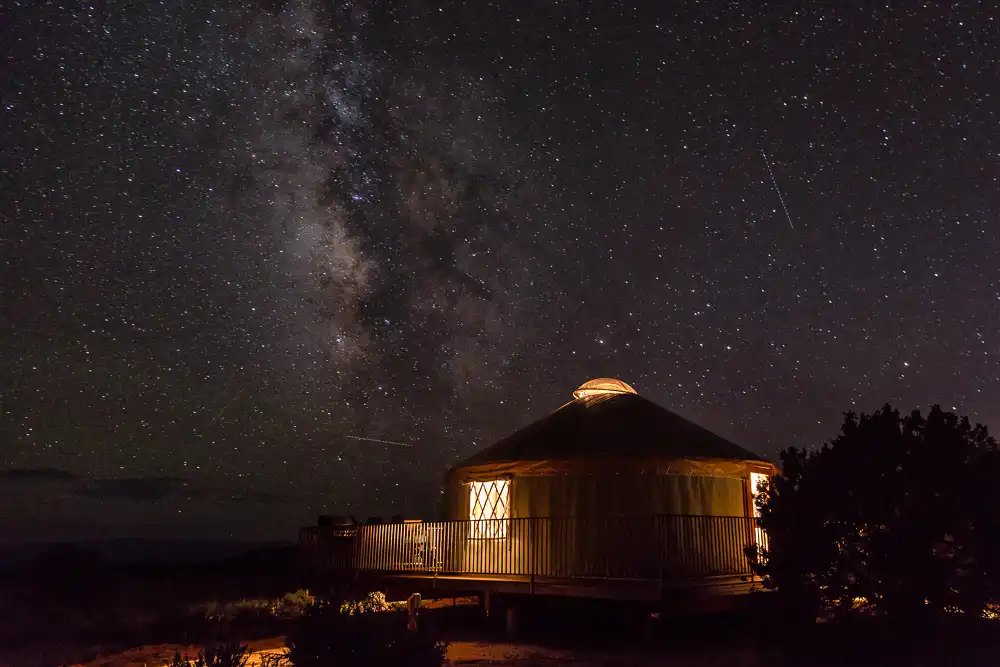 Yurt with glowing windows under a starry night sky and visible Milky Way.