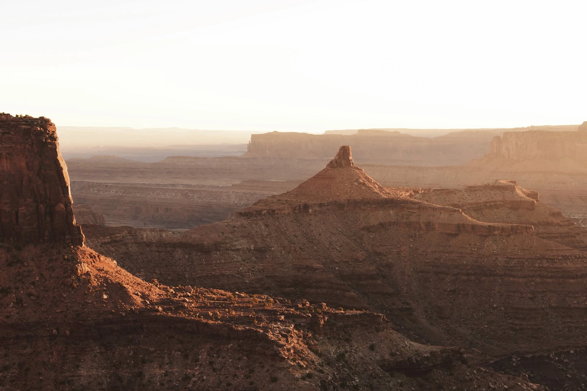 Sunlit mesas and canyons in a desert landscape during sunset.