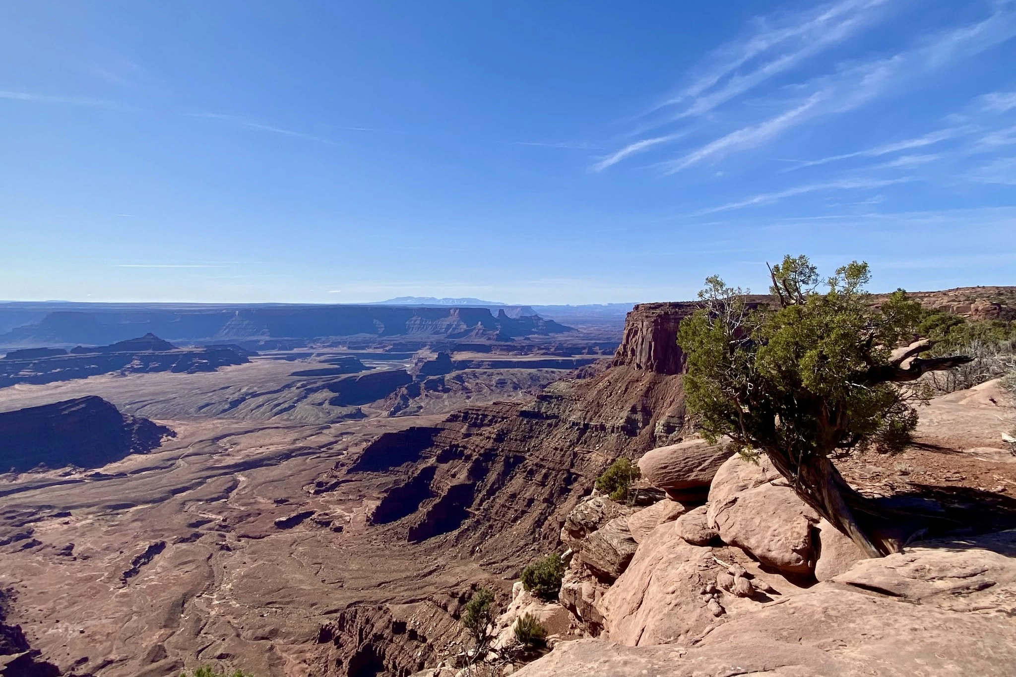 Desert canyon landscape with rocky cliffs, sparse vegetation, and a clear blue sky.