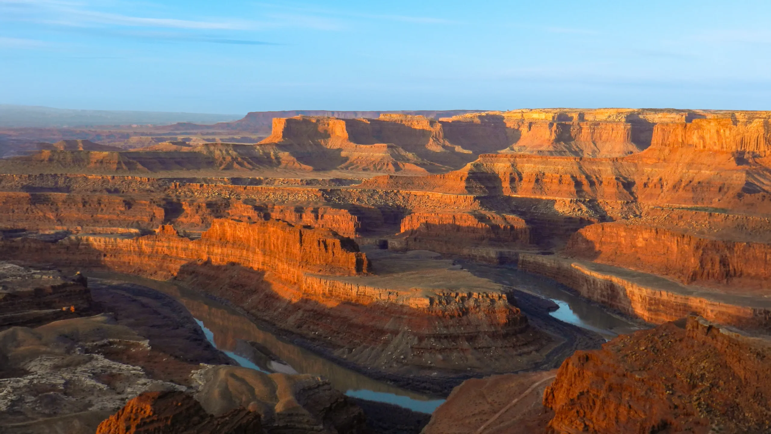 Canyon landscape with red rock formations and a winding river under a blue sky.