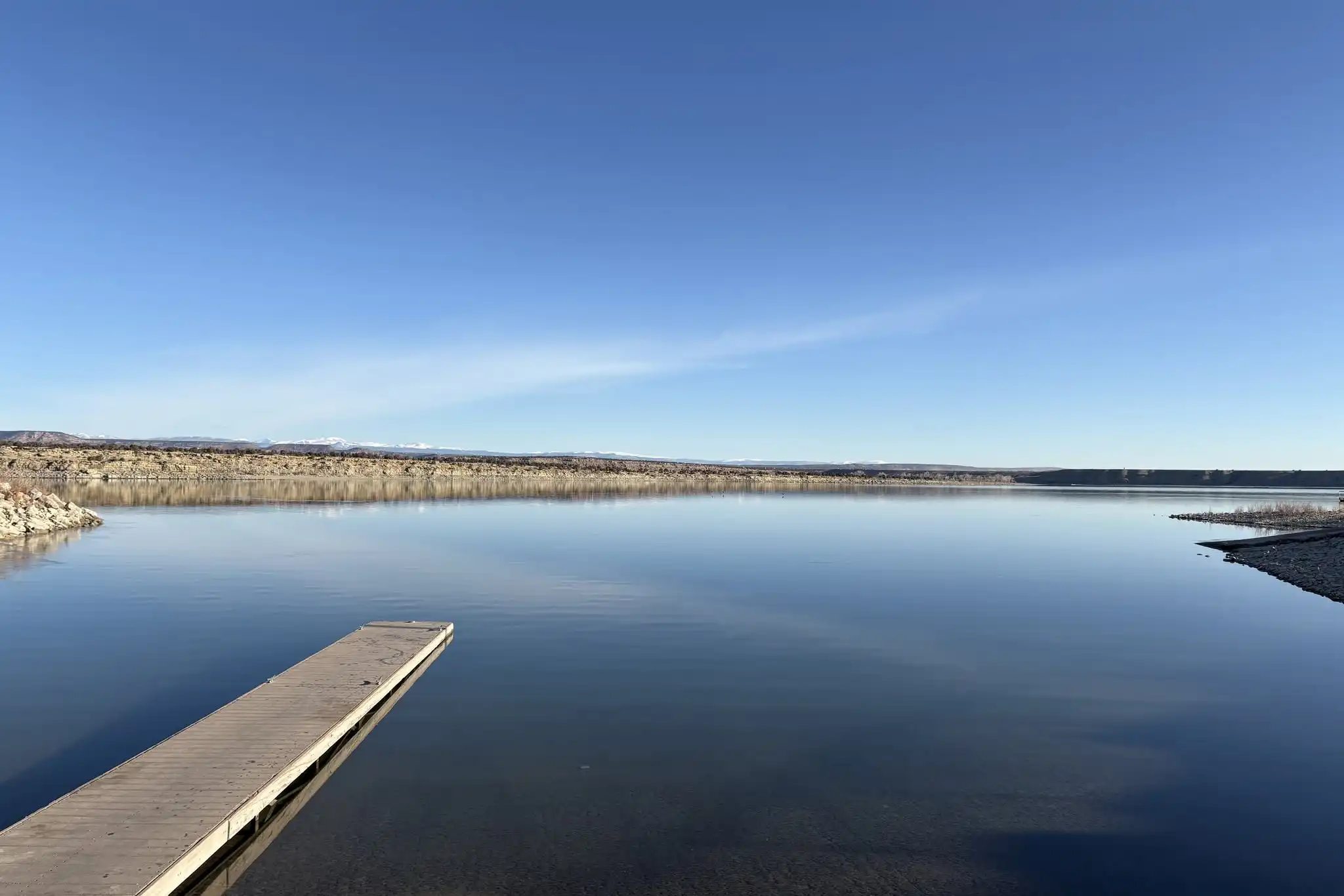 Wooden dock extends over a calm lake with clear sky and distant shoreline in view.