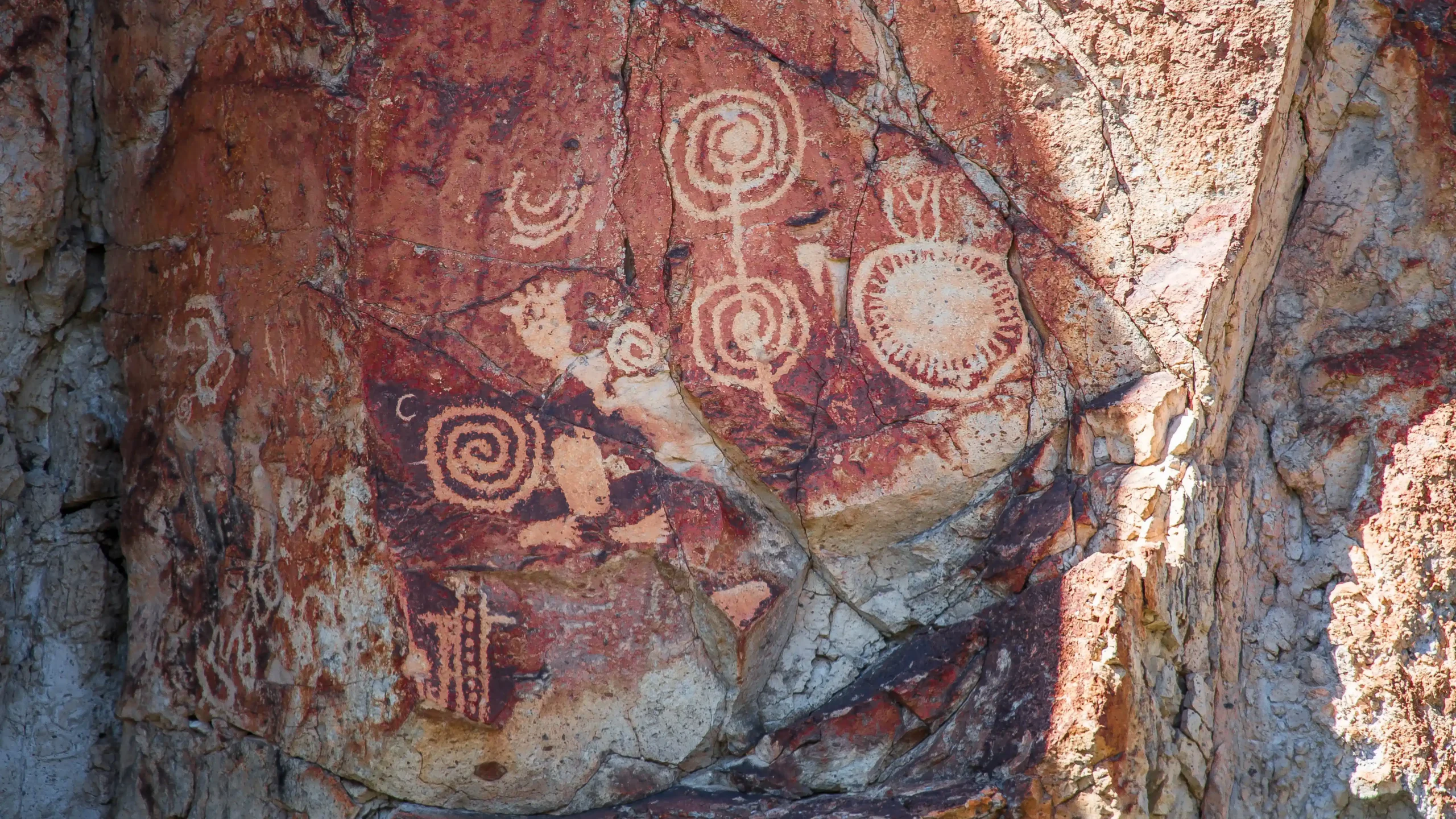 Ancient rock with spiral and circular petroglyphs carved into a reddish stone surface.