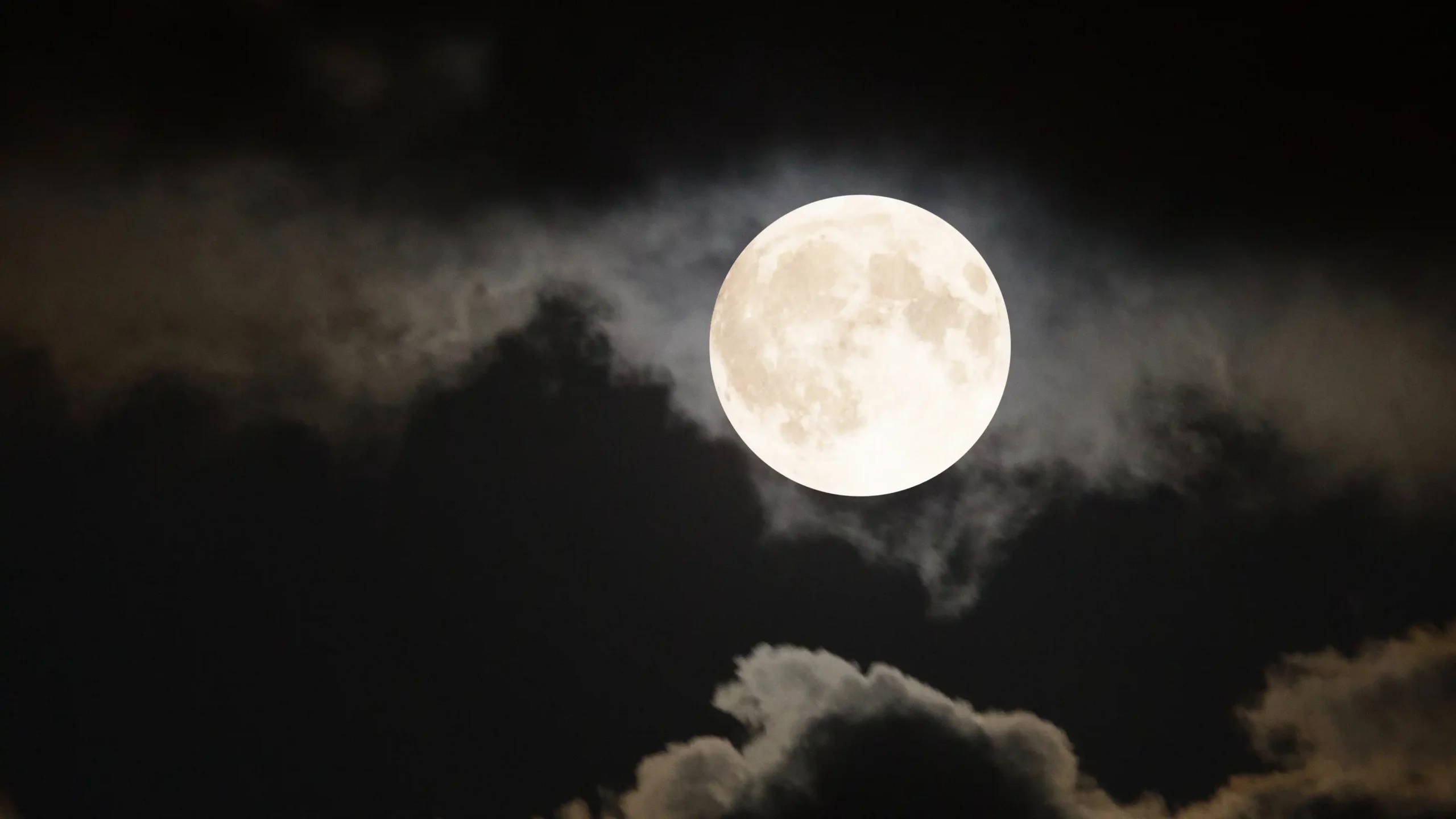 Full moon glowing in a dark night sky with clouds partially surrounding it.