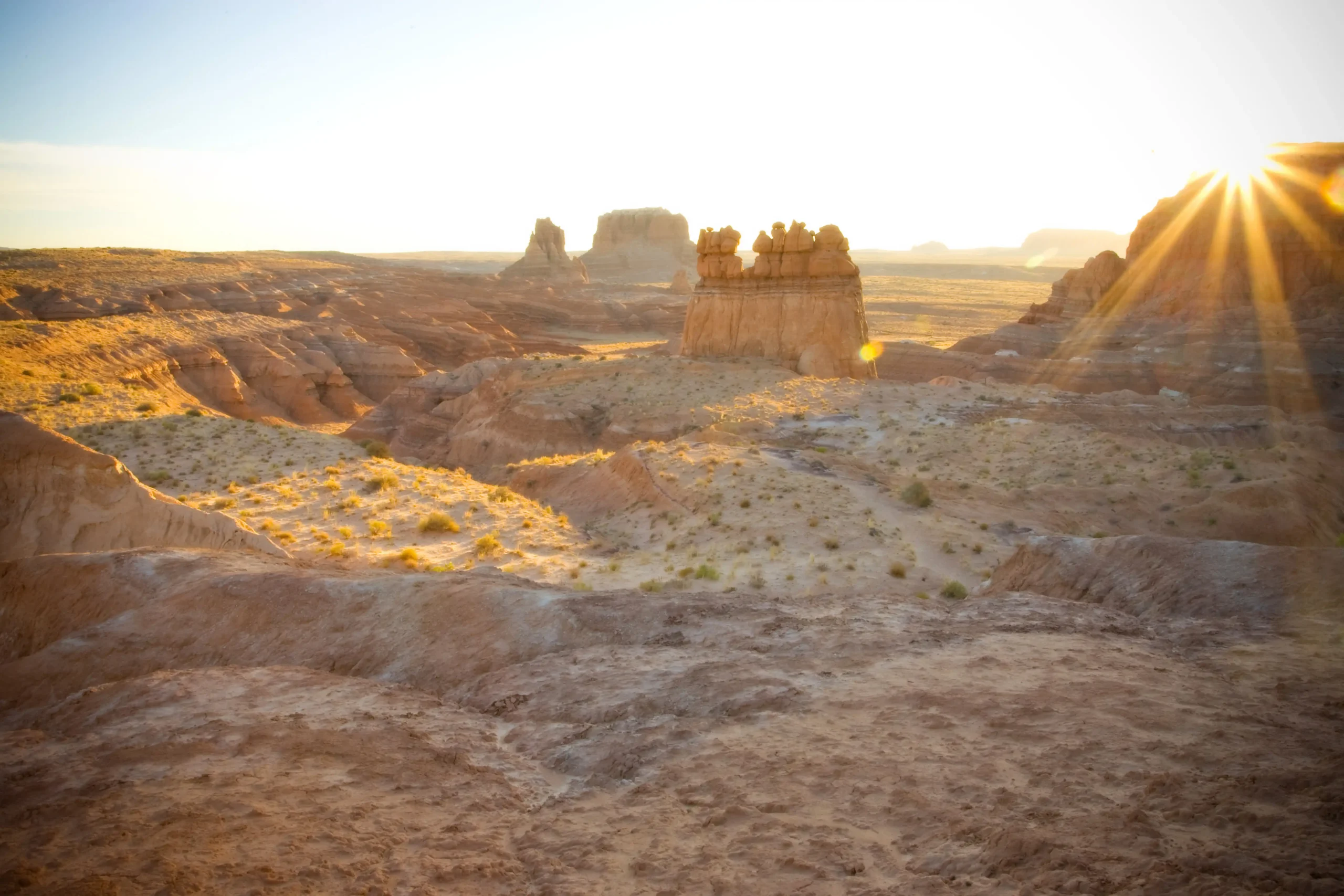 Sunrise over a rocky desert landscape with mesas and scattered shrubs.