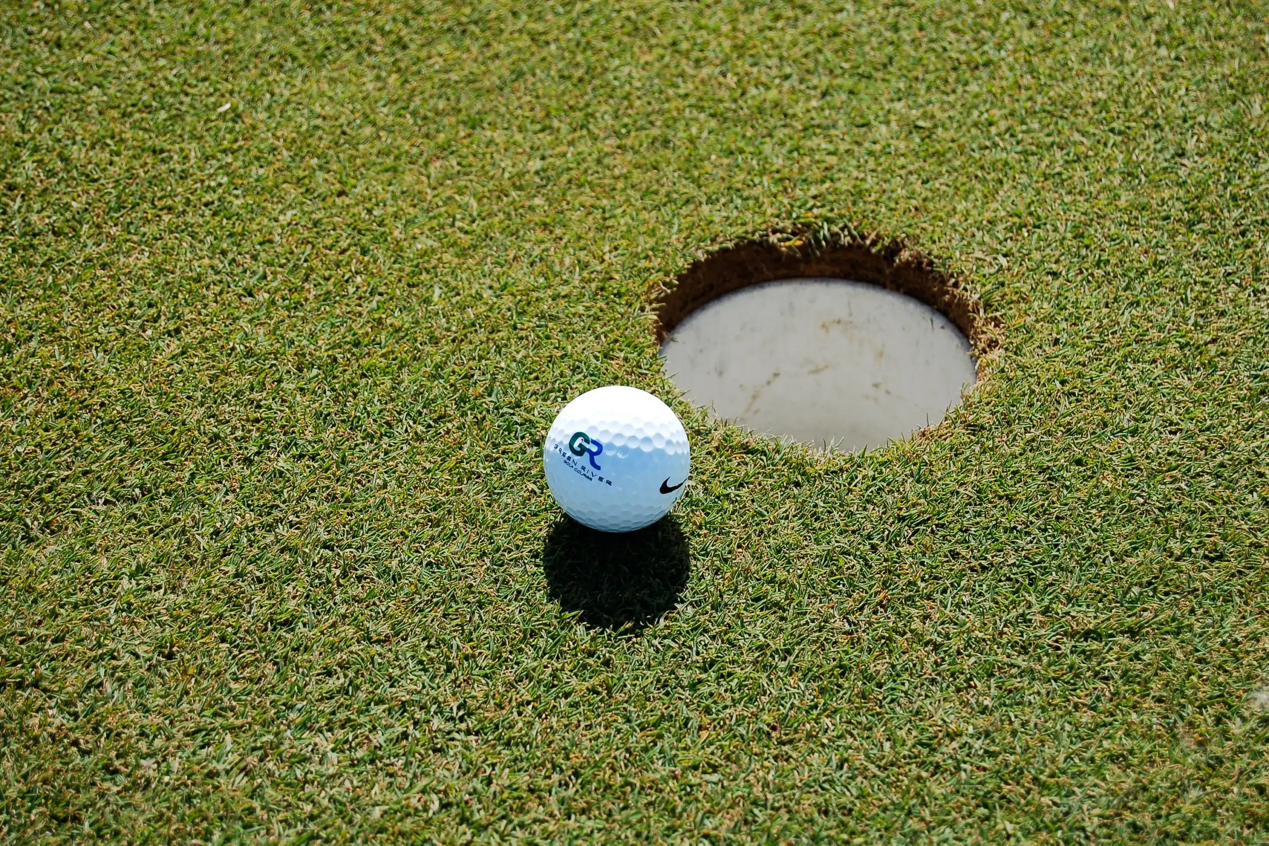 A golf ball rests on the green next to a hole on a golf course.