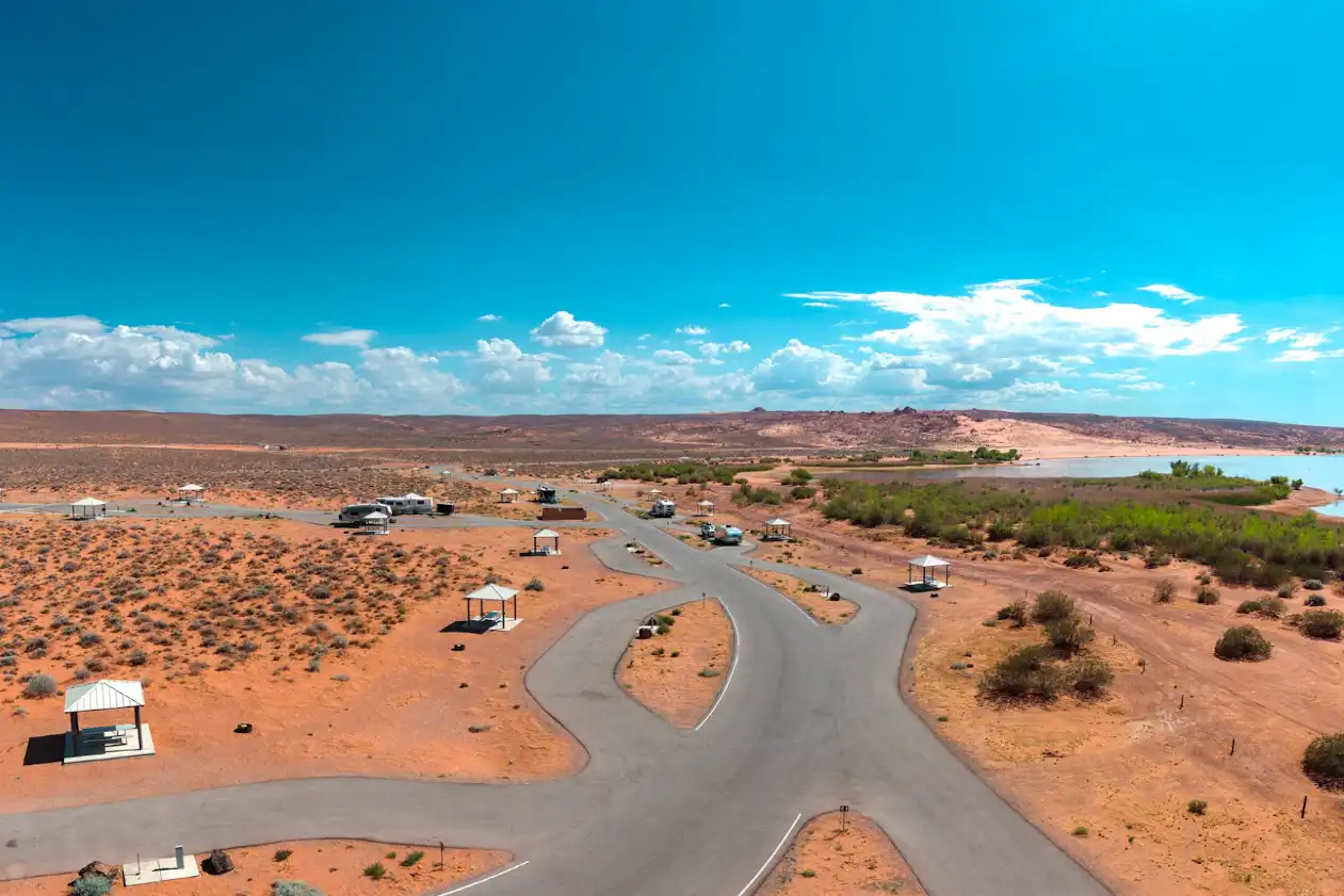 Aerial view of a desert campground with scattered shelters and a winding road under a blue sky.
