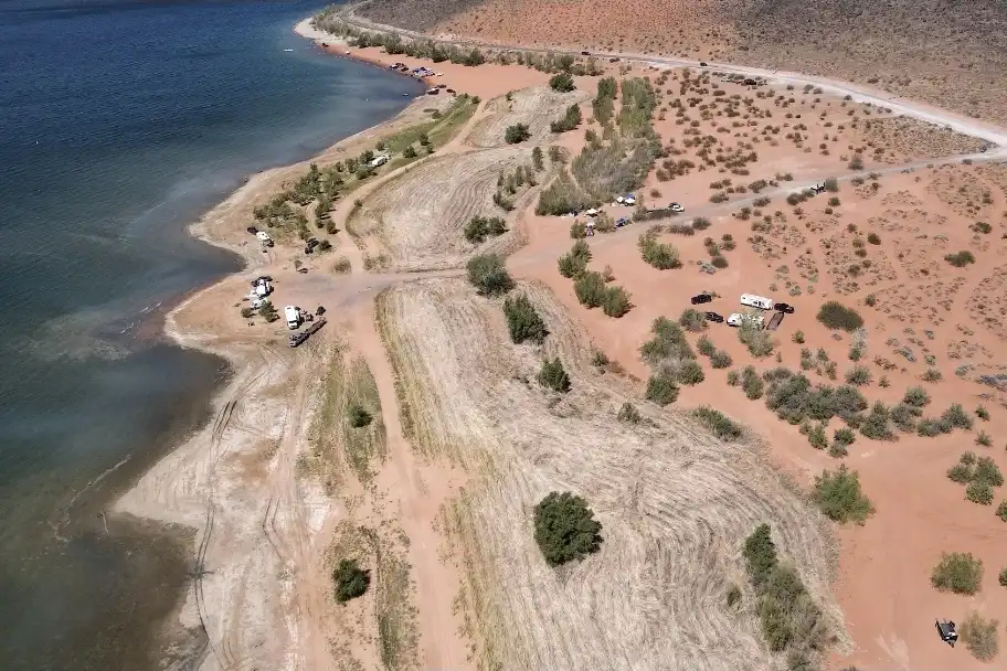 Aerial view of a lakeshore with cars, tents, dry grass, and scattered bushes.