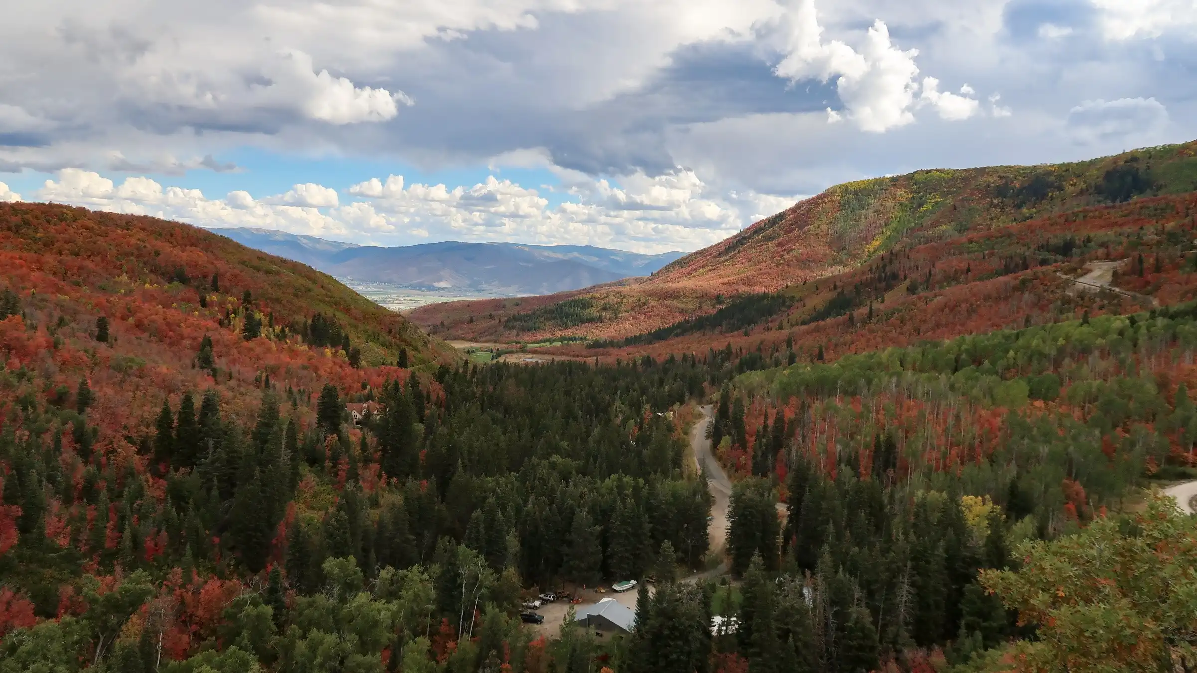 Mountain valley with trees in fall colors under a partly cloudy sky.
