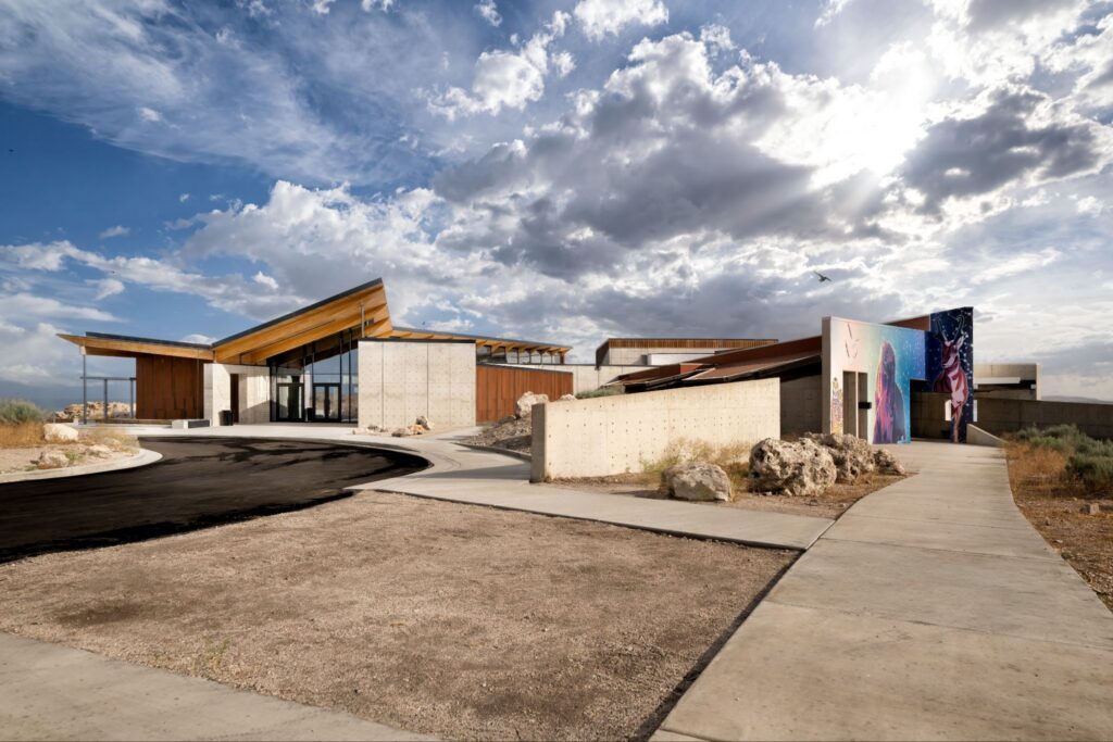 Modern building with angular roof, concrete walls, and colorful mural under a cloudy sky.